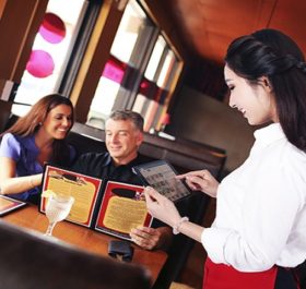 Happy mature waiter taking order from couple at restaurant