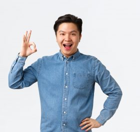 Satisfied confident smiling asian guy with braces, showing okay gesture, recommend perfect doctor clinic, great stomatology, being pleased with results, standing white background amazed.